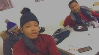 Three people sitting indoors, wearing winter clothing and looking toward the camera.