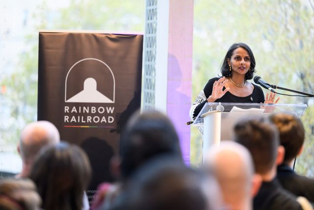 Person speaking at a podium during a Rainbow Railroad event with the organization’s banner beside them.