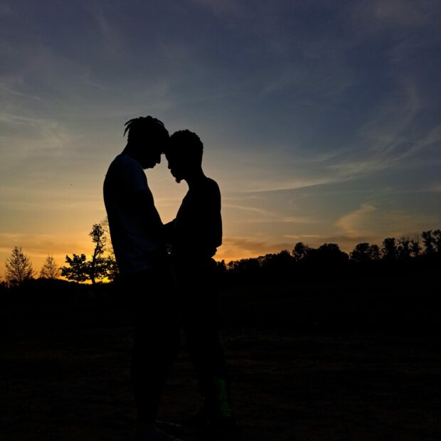 Two people standing close in silhouette at sunset.