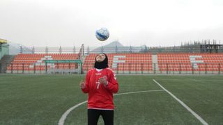 Person in a red jersey tossing a soccer ball on a field.
