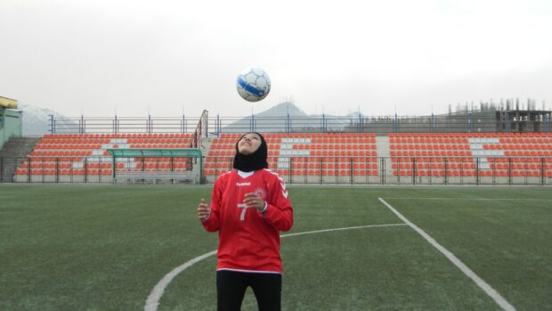 Person in a red jersey tossing a soccer ball on a field.