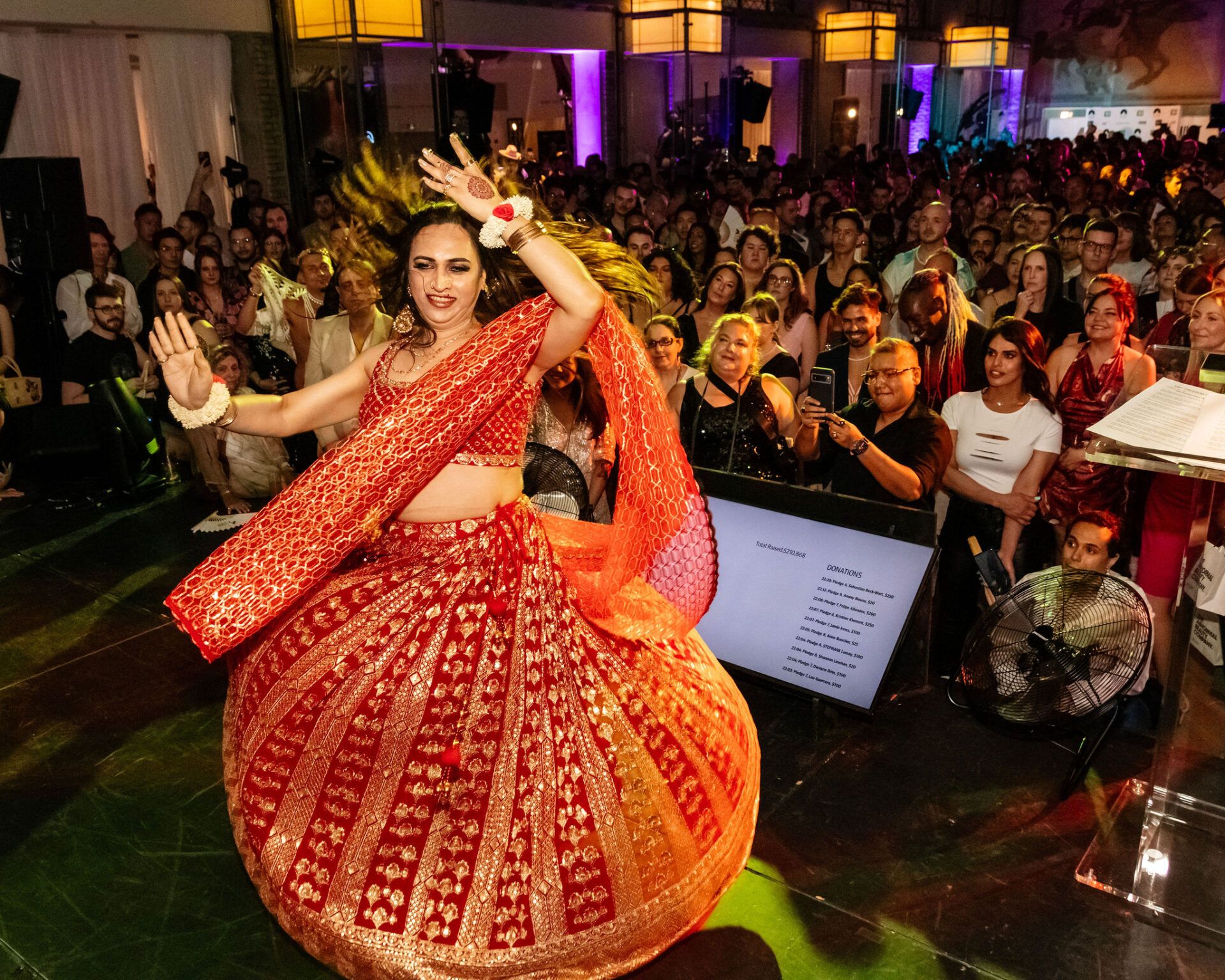 Person in a red and gold traditional dance outfit performing onstage.