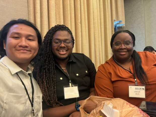 Three people smiling and seated at a conference table.