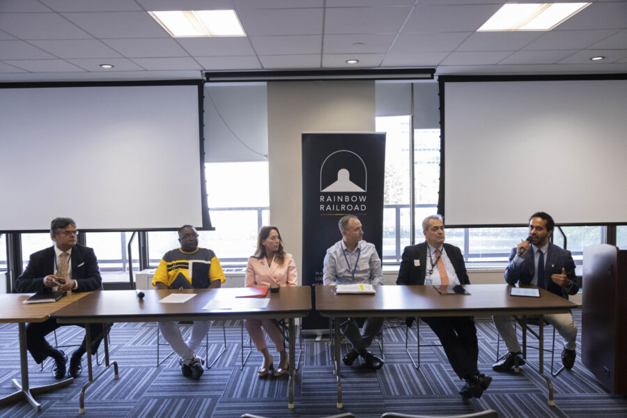A panel of six people speak at a long table during a Rainbow Railroad event.