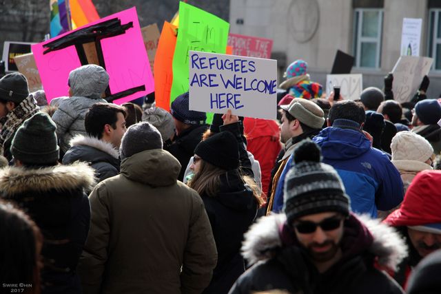 Crowd in winter clothing holds signs, including one reading “Refugees Are Welcome Here.”