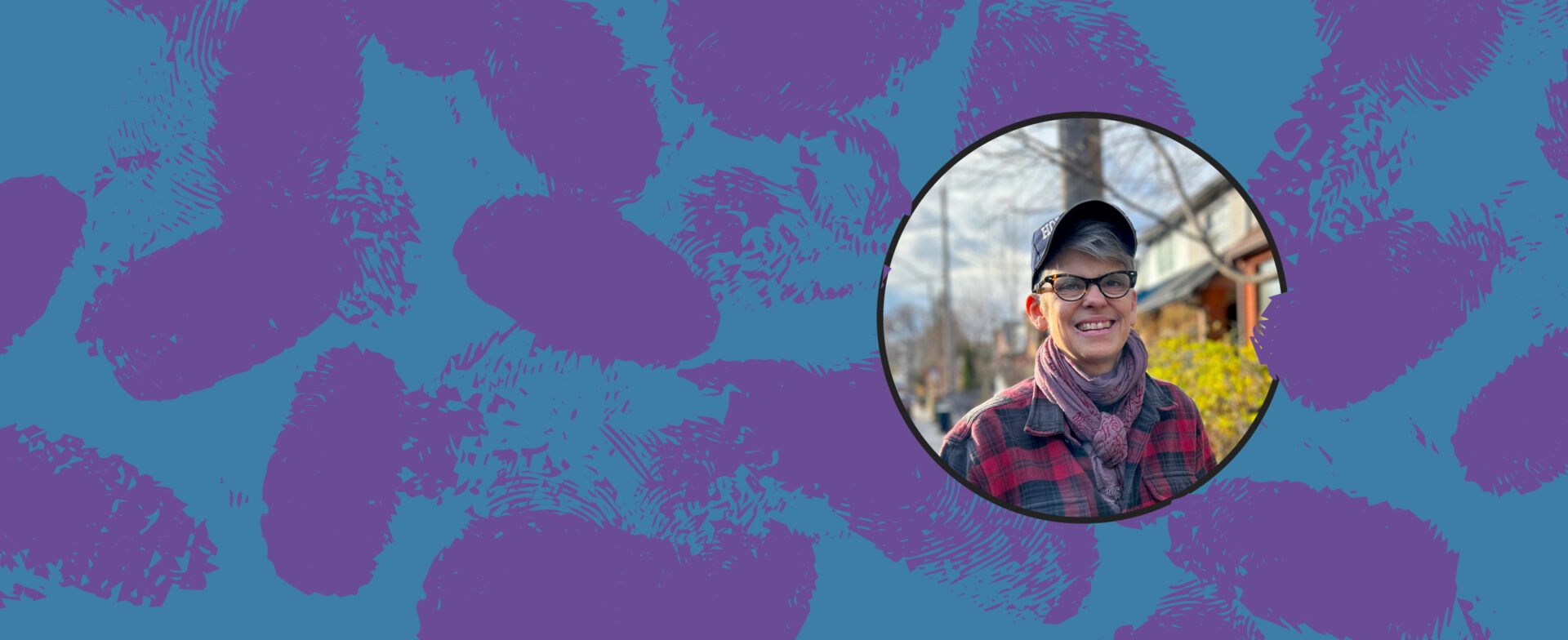 Person smiling outdoors wearing glasses, a cap, and a scarf.