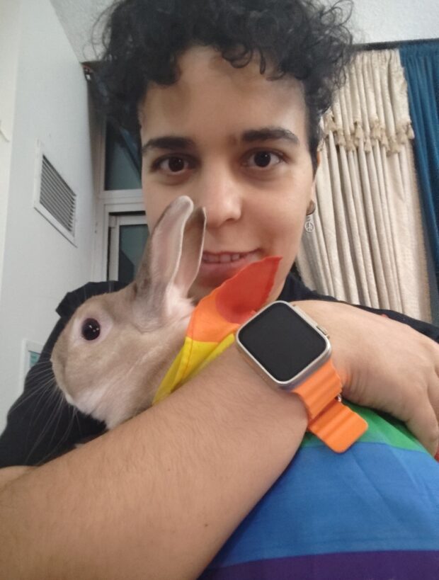 Person smiling and holding a rabbit wrapped in a rainbow flag.