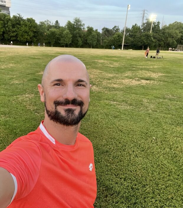 Person in an orange shirt against a grassy background with trees.