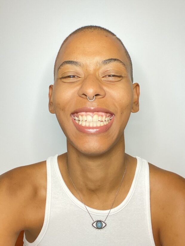 Person smiling against a plain background, wearing a white tank top.