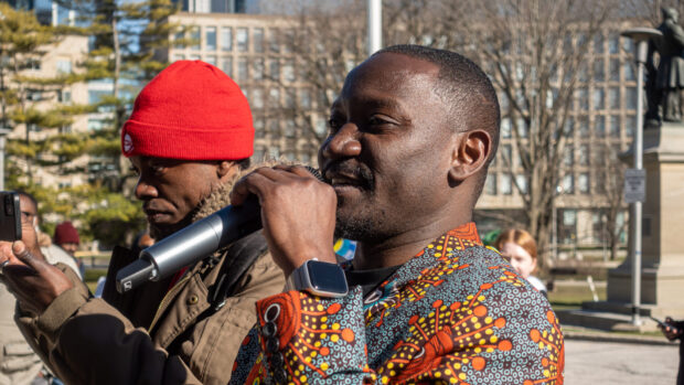Person speaking into a microphone at an outdoor gathering.