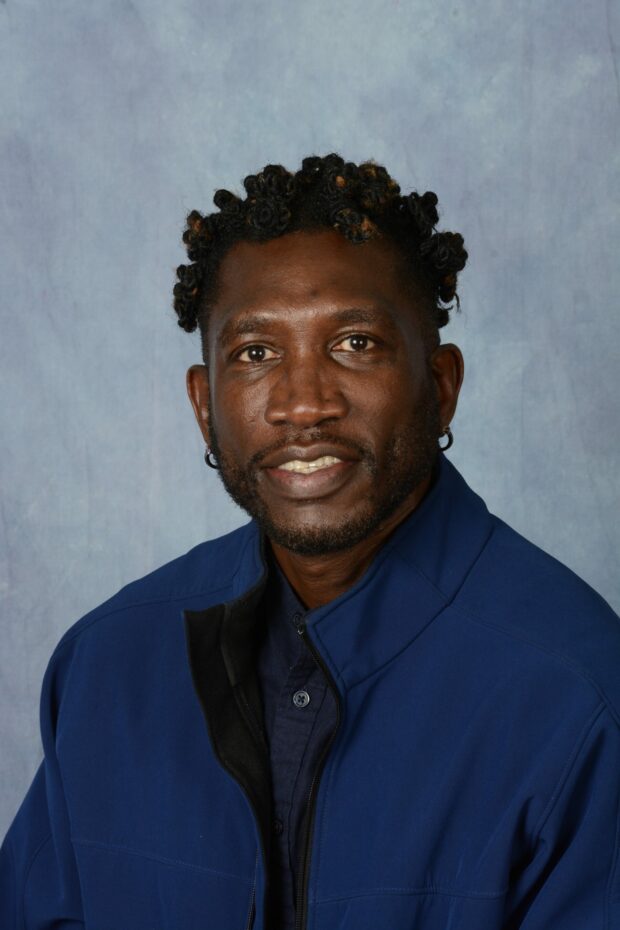 Portrait of person with curly black hair and a navy jacket.