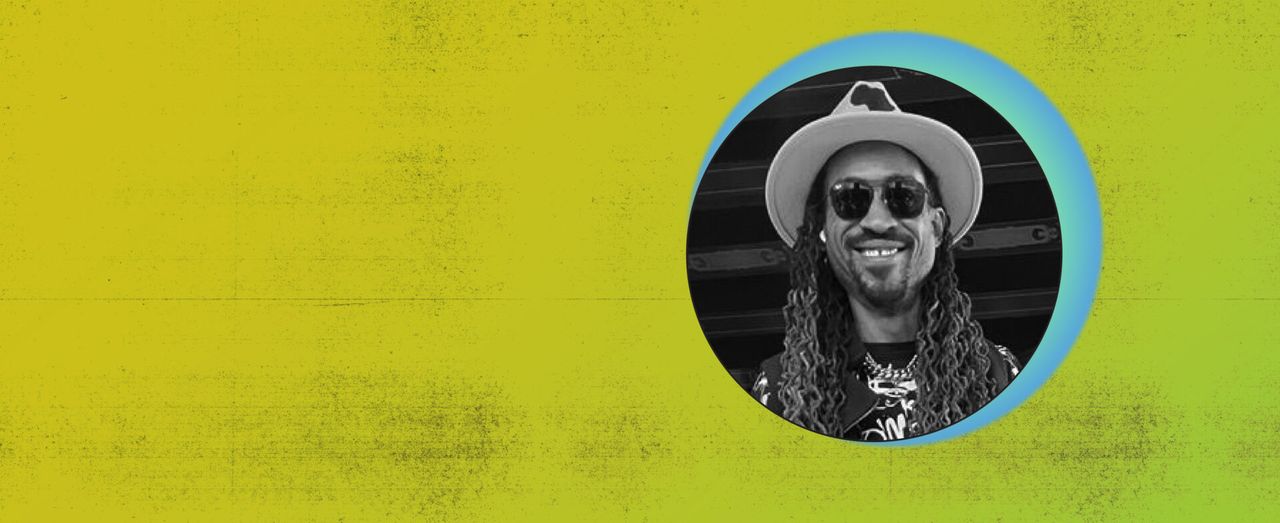 Black-and-white portrait of a smiling person in a hat and sunglasses on a yellow background.