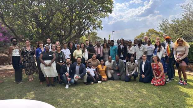 Group of people posing together outdoors on a sunny day with trees and grass in the background.