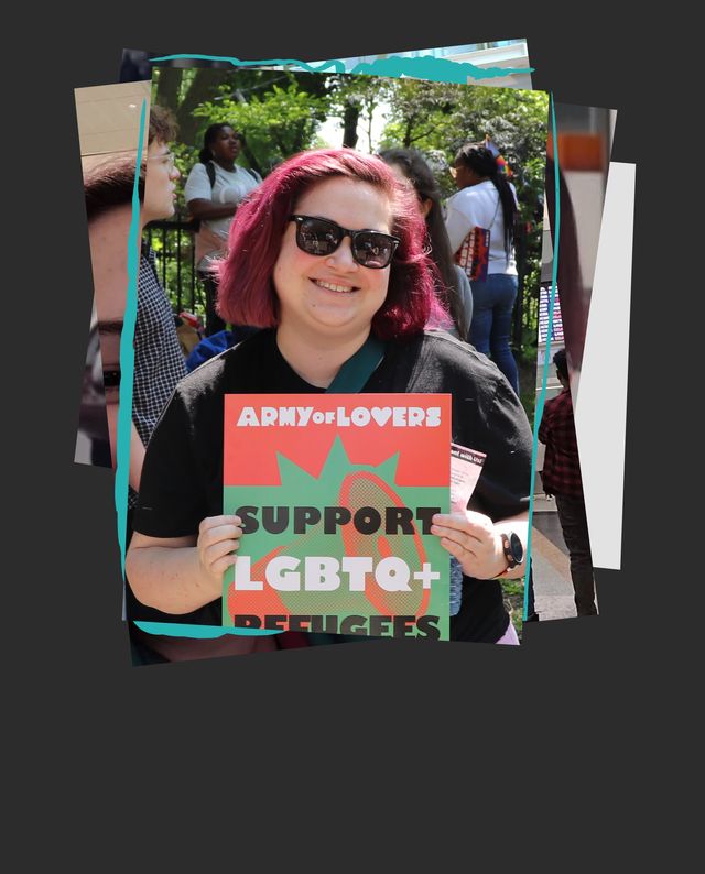 Person with pink hair holding a sign reading ‘Support LGBTQ+ Refugees’ outdoors with people in the background.