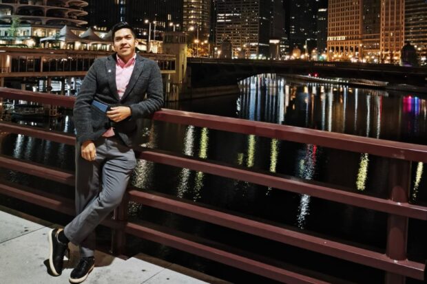 Person posing on a bridge at night with city lights reflecting on the river behind them.