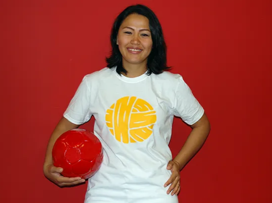 Person smiling and holding a red soccer ball while standing against a red wall.