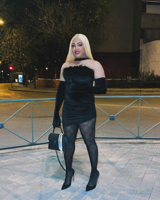 Person in a black dress and gloves posing outdoors at night.