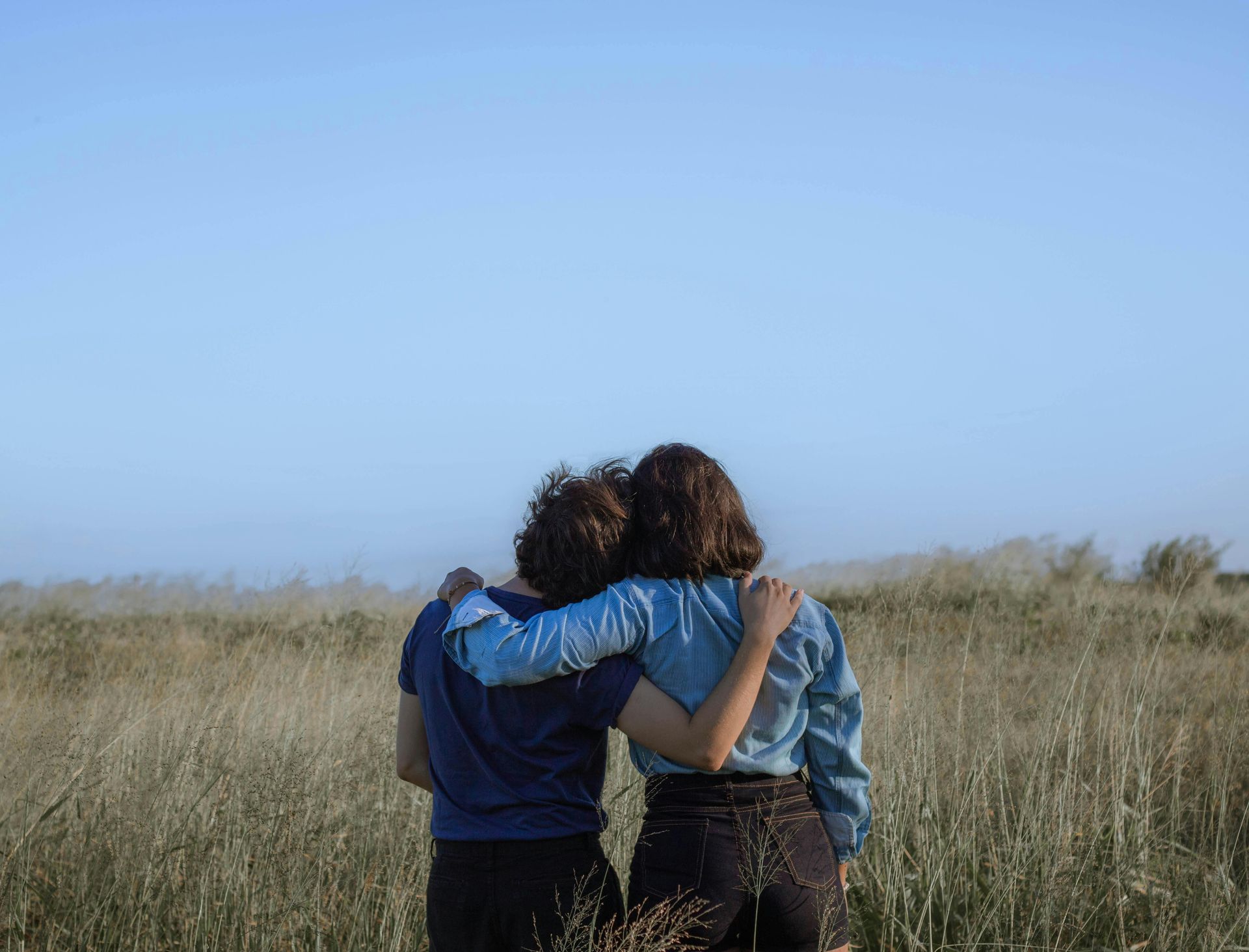 People side hugging in field from back